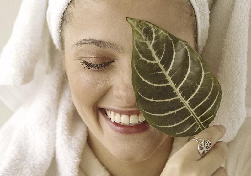 Woman in spa robe laughing with leaf over her face